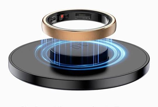 Gold-tone smart ring floating above a black round wireless charging pad with blue rings of light