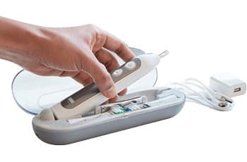 Hand placing a toothbrush into a grey semi-hard travel case with a charging cable and plug inside