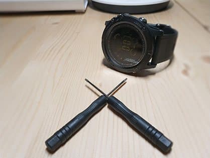 Two small black screwdrivers on a wooden table in front of a T-Watch, offered as the T-Watch Screwdriver add-on