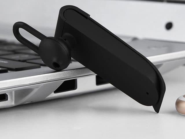 Black TranslateTrek earpiece with a silicone ear tip and loop resting against the edge of a silver laptop