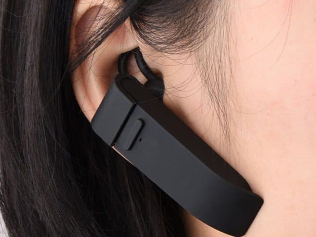 Close-up of the black TranslateTrek hooked over a person's ear, with a button on its side