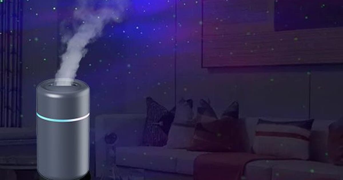 Grey TwilightMist humidifier with a blue light ring releasing a plume of mist in a dark living room lit with purple and blue starry light
