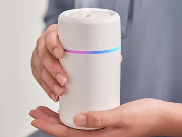 Hands holding a white TwilightMist cup with a thin rainbow-coloured light band around its middle