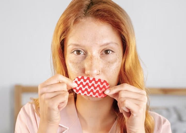 Woman holding a red patterned Ugly Sleep Club strip up to her lips