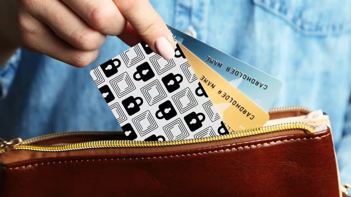 Hand placing a Wallet Defender card into a red purse beside a gold credit card