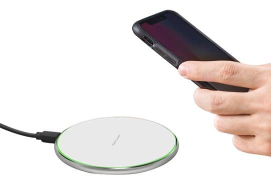 Winergy white charging pad with a silver metal rim glowing green at the edge, cable attached, and a hand holding a phone above it