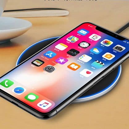 An iPhone lying on a black round wireless charger with a blue light ring, on a wooden desk, used for the Winergy smart lights add-on