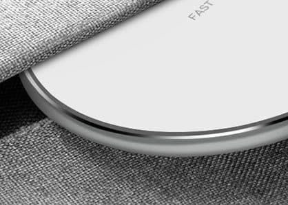 Close-up of the edge of a white wireless charging pad with a polished silver rim, resting on grey fabric