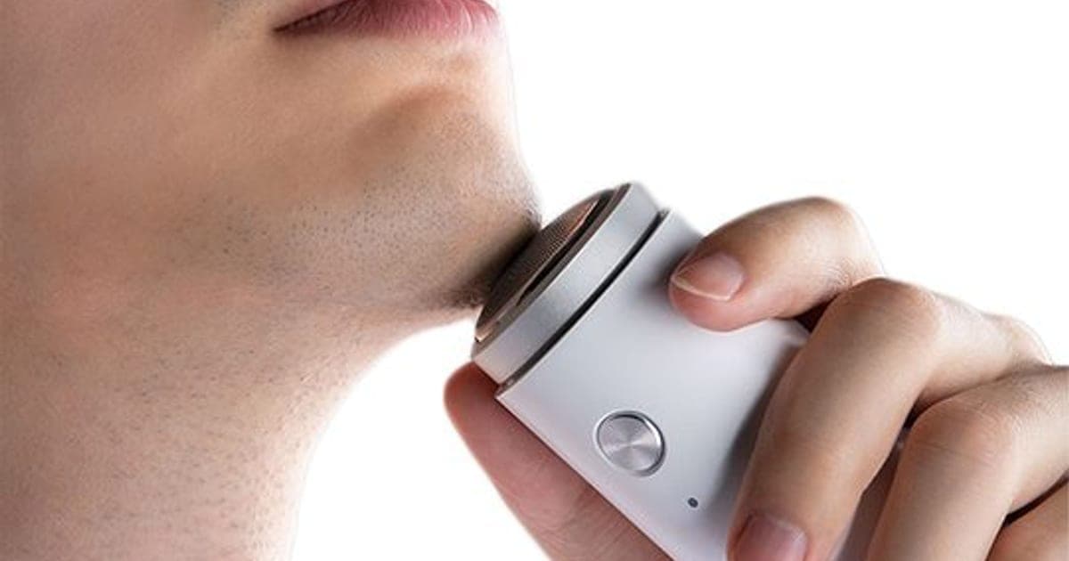 Hand holding a small white ZeroShave Pro shaver with a round metal foil head against a man's stubbled chin