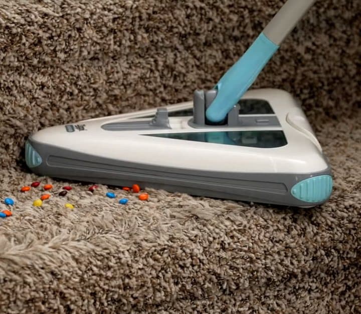 Zippi Sweeper on a thick brown carpet with scattered coloured debris