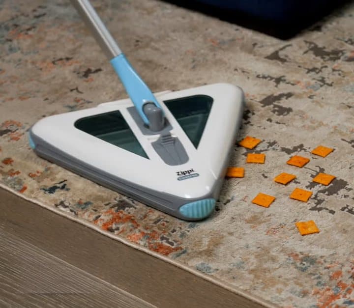 Zippi Sweeper picking up orange debris from a patterned rug