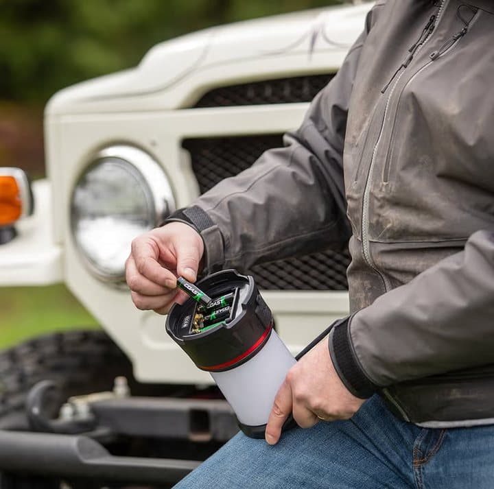Person loading Zithion-X batteries into a camping lantern beside a vehicle