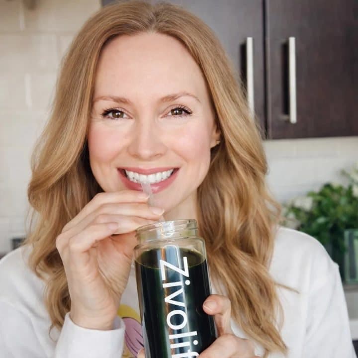 Woman smiling while holding a glass of green Zivolife drink
