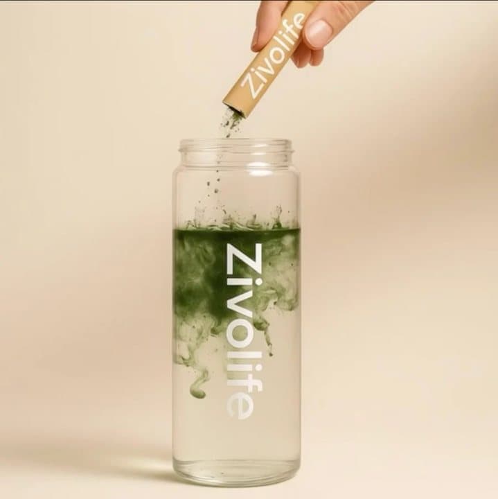 Hand pouring a Zivolife stick of green powder into a glass of water