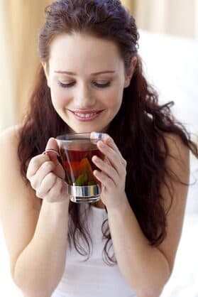 Woman smiling as she holds a glass mug of herbal tea