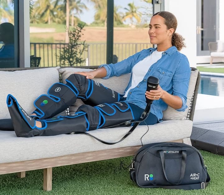 A woman relaxing on an outdoor sofa wearing the Air-C leg massager, with its carry bag beside her