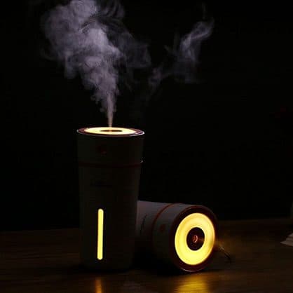 Two cup-shaped humidifiers glowing warm amber in a dark room, one standing and misting, one lying on its side, used for the night light add-on