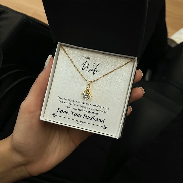 Hand holding an open box with the gold-tone Alluring Beauty ribbon pendant on the same To My Wife card
