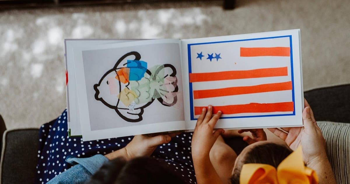Parent and child reading an Artkive hardcover book showing a child's fish drawing and flag painting