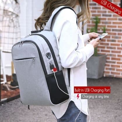 Woman wearing the grey BackXPack while her phone charges through a cable from the side USB port, labelled built-in USB charging port