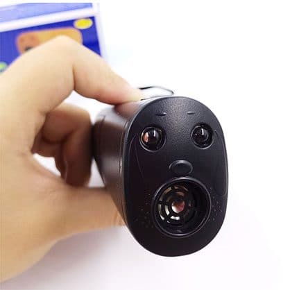 Front of a black handheld ultrasonic device with two LED lenses above a round speaker grille, held in a hand, used for the BarXStop wide frequency speaker add-on