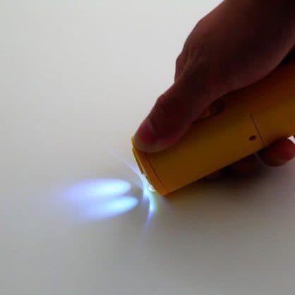 A hand holding a yellow handheld device shining two white LEDs onto a table, used for the BarXStop torch add-on