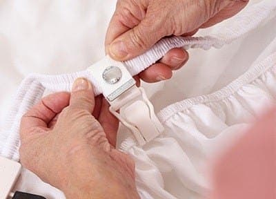 Hand attaching a white Bed Scrunchie clip to the edge of a white fitted sheet