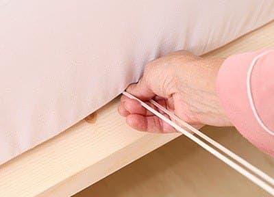 Hand pulling the Bed Scrunchie drawcord from under the foot of a mattress on a wooden bed frame