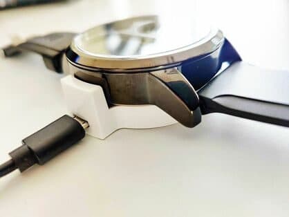 BiT Watch resting in a white charging dock connected to a USB cable, seen side-on