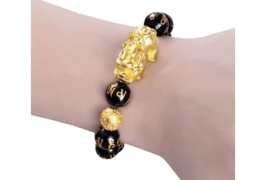 Wrist wearing a stretch bracelet of large black beads with gold mantra carvings, a gold Pixiu figure and a gold patterned bead