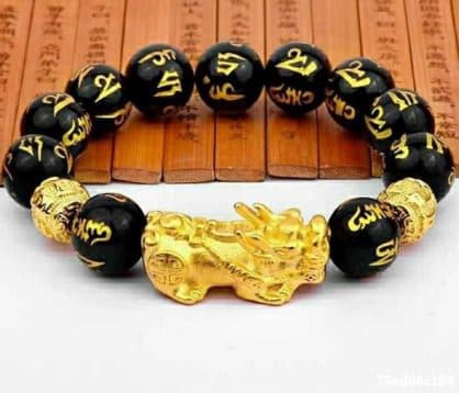 Bracelet of large black beads with gold characters, two gold beads and a gold Pixiu charm, laid on wooden slats