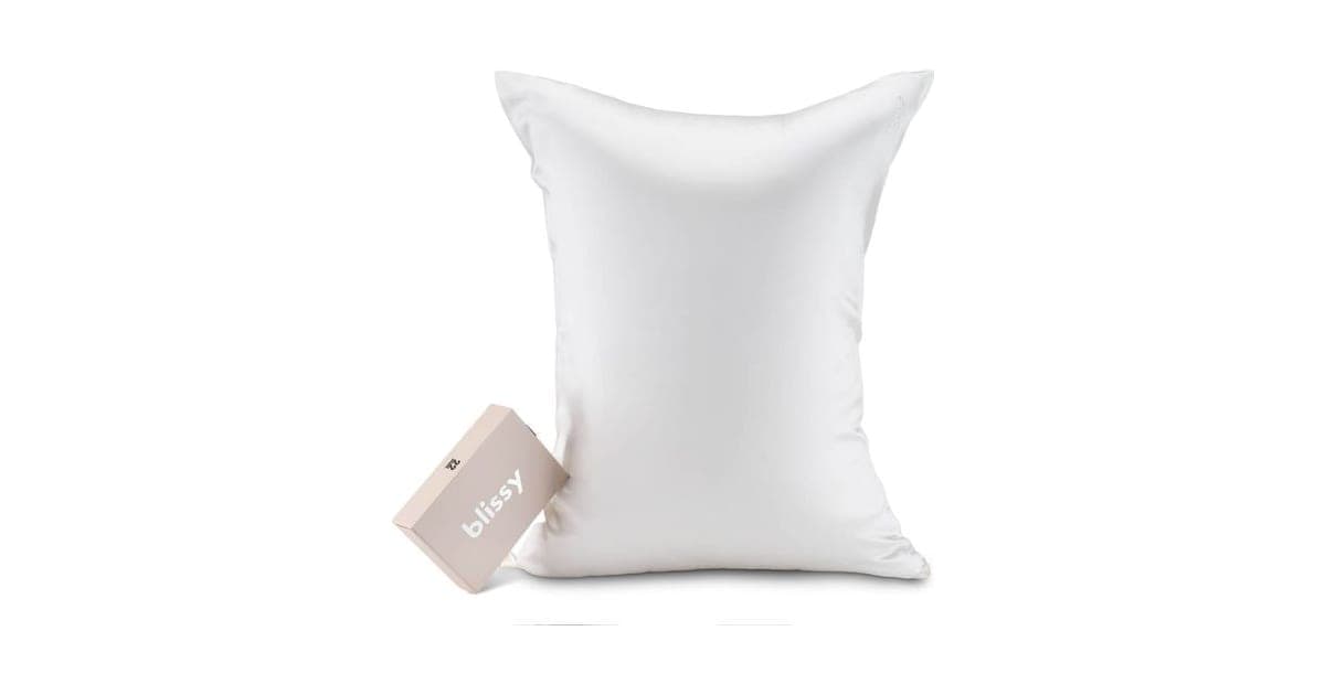 White Blissy mulberry silk pillowcase on a pillow beside its pale pink Blissy gift box, on a white background