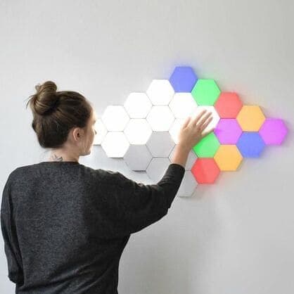 A woman touching a wall of white and coloured hexagon lights in blue, green, red, orange and purple