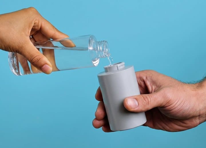 Hand pouring water from a bottle into the BumBum bidet's water canister