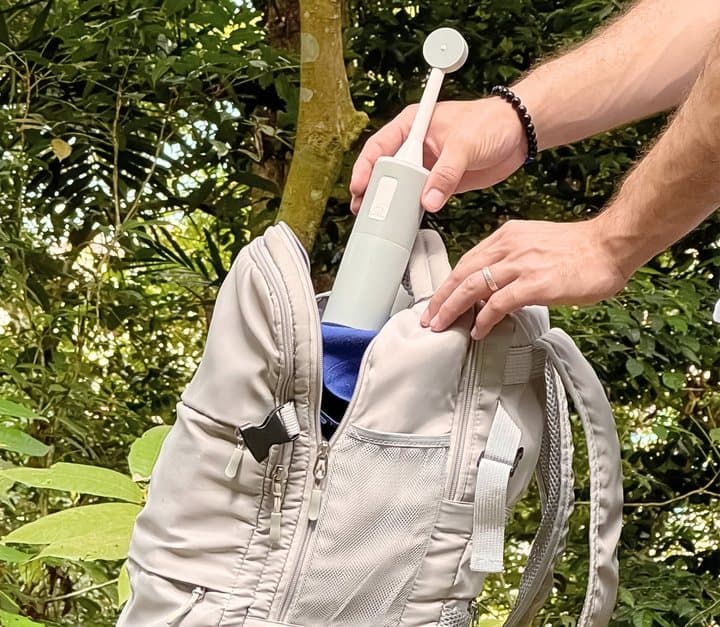 Hand putting the BumBum bidet into a backpack outdoors