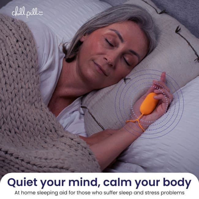 Older woman asleep in bed holding the orange Chill Pill with its strap around her wrist