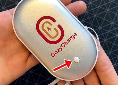 Hand holding the CozyCharge with a red arrow pointing to its single power button