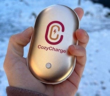 Hand holding the silver CozyCharge outdoors against a snowy background