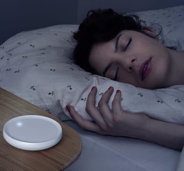 Woman sleeping on a pillow beside a softly glowing Dodow sleep light in a dark bedroom