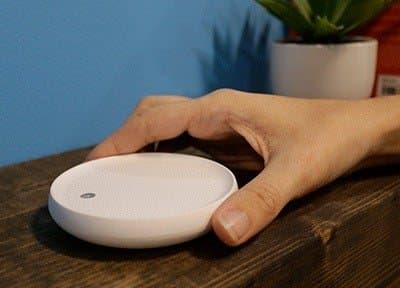 Hand tapping the top of a Dodow sleep light on a wooden nightstand to start a cycle
