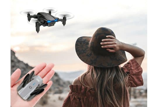 Small black DroneXS hovering with blue lights against a sunset sky, and a folded grey version resting in someone's palm