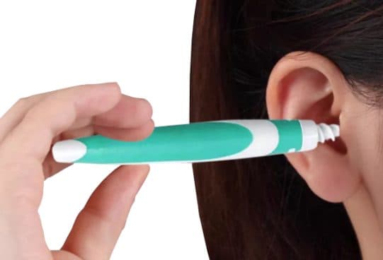 Teal and white Easy WaxOff handle with a white rubber spiral tip held at the entrance to a woman's ear canal