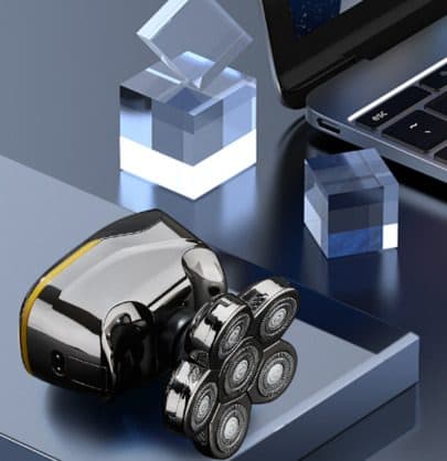 ElectricShaver Pro in black and gold with six round rotary heads, resting on a dark surface beside glass cubes and a laptop