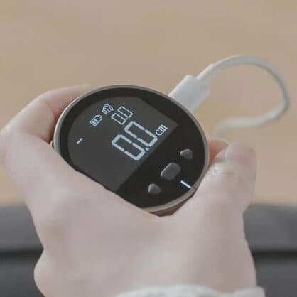 Hand holding the ElectronX Ruler showing 0.0 cm while a white USB-C cable charges it