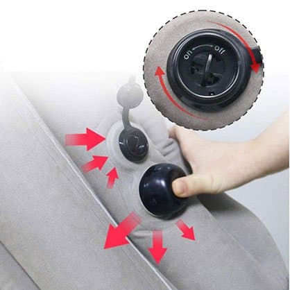 Hand pressing a round black pump button beside a twist valve on a grey ErgoRelax pillow, with red arrows showing airflow