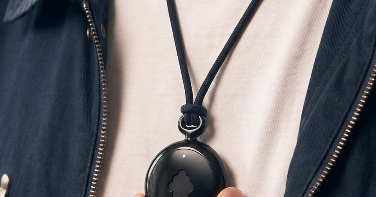 Black Fieldy AI pendant worn on a cord over a white shirt, with a finger pressing its button