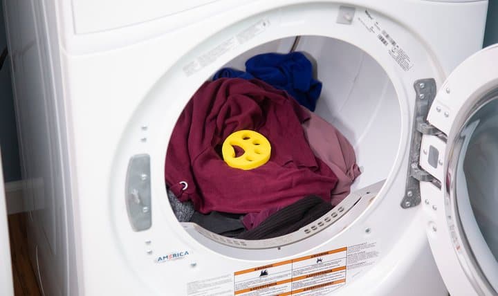 Yellow FurZapper disc on top of red clothes inside a front-loading washing machine drum