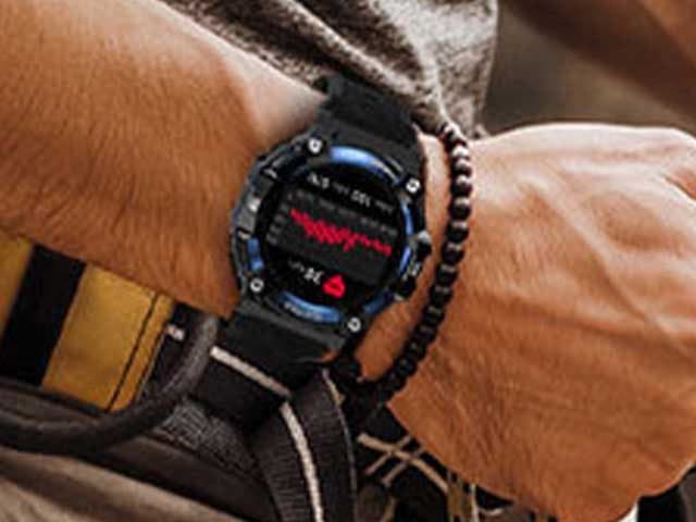Wrist wearing a black and blue rugged smartwatch on a strap, showing a heart rate graph, beside a bead bracelet