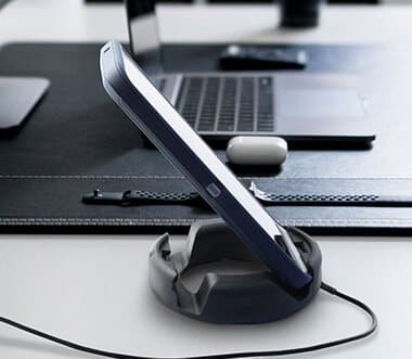Phone standing in a dark GoDonut on a desk with a charging cable running through the stand