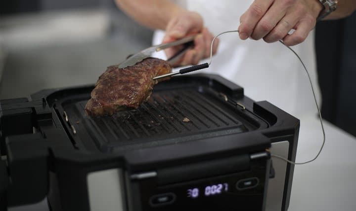 Steak on the Gourmax Pro grill plate with the temperature probe inserted and tongs nearby